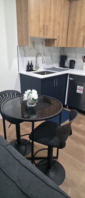 A modern kitchen with wooden cabinets, a marble countertop, a sink, and a dining area with a glass table and black chairs. - New Cozy One bed Suite  close to downtown Edmonton.For Leisure and Business Stay (Northwest)