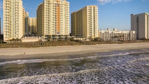 Um hotel à beira-mar com vários edifícios altos, uma praia de areia e ondas do oceano.