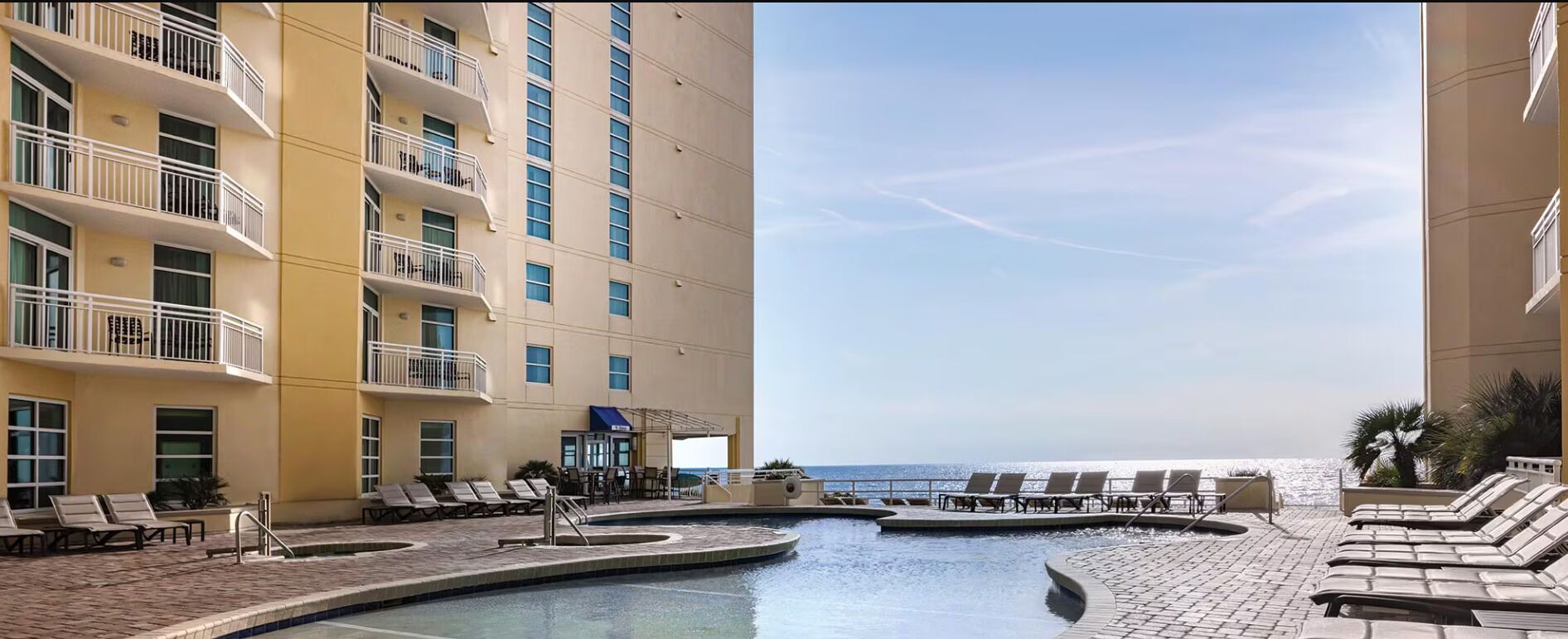 Ein Hotelpoolbereich mit mehreren Liegestühlen, einem Pool und Blick auf den Ozean.