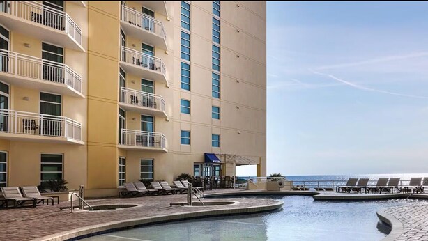 Uma área de piscina de hotel com várias espreguiçadeiras, uma piscina e vista para o oceano.