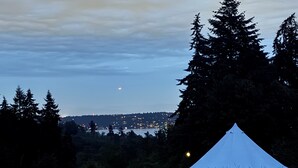 Una carpa en un campo de hierba con vistas a un horizonte urbano lejano y la luna en el cielo.