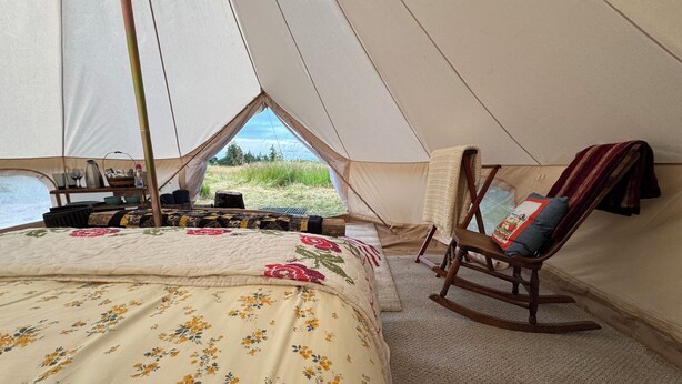 Una carpa con cama, una mecedora y vistas al exterior.