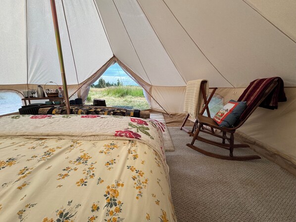 A tent with a bed, a rocking chair, and a view of the outdoors.