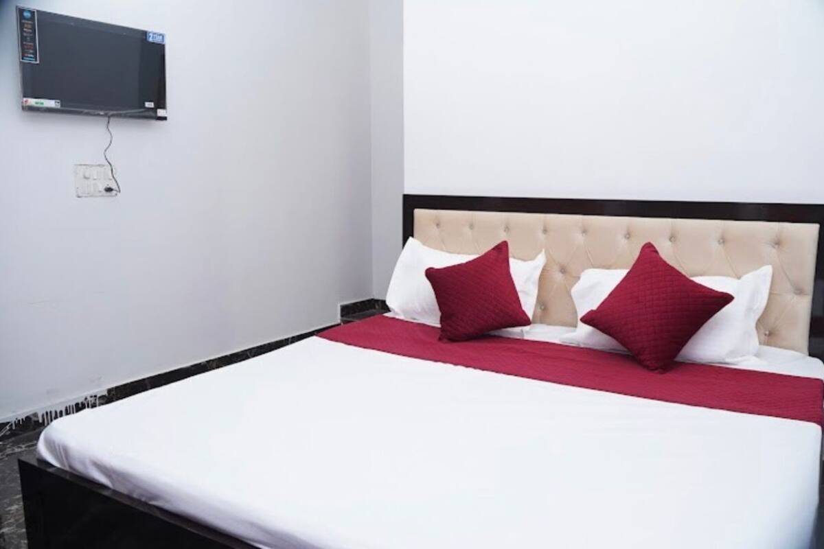 Un lit avec une tête de lit capitonnée, deux oreillers rouges et un couvre-lit blanc.