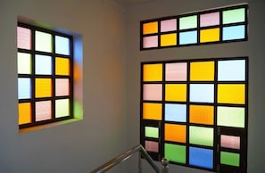 A staircase with a handrail and two windows with colorful stained glass panels. - Shri daulat villas hotel (Udaipur)