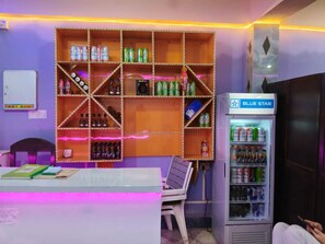 Una habitación con una estantería que contiene diversas bebidas, una mesita con una silla y un refrigerador con el rótulo 'BLUE STAR'.