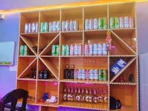 A shelf with various beverages, including cans and bottles, in a room with a chair and a key box.