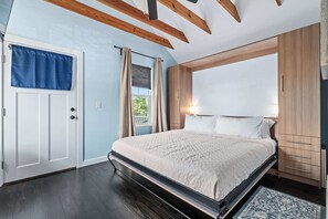 Et soveværelse med seng, træbjælker i loftet, et klædeskab og et vindue med gardiner.
