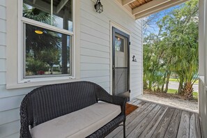 A porch with a wicker sofa, a door, and a window overlooking a garden. - Lincolnville Charm l Walk to DNTN l Dog Friendly (St. Augustine)