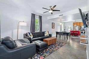 Ein modernes Wohnzimmer mit Sofa, Hocker, Couchtisch und einem Essbereich mit Stühlen und Tisch.