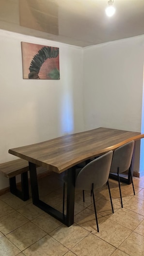 A dining area with a wooden table and four chairs, a bench, and a painting on the wall. - Chez AUBADE house in Bras Sec (Cilaos)