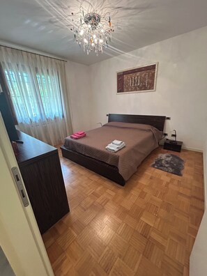 Ein Schlafzimmer mit einem Bett, einer Kristallleuchtre, einem Gemälde und Holzboden.