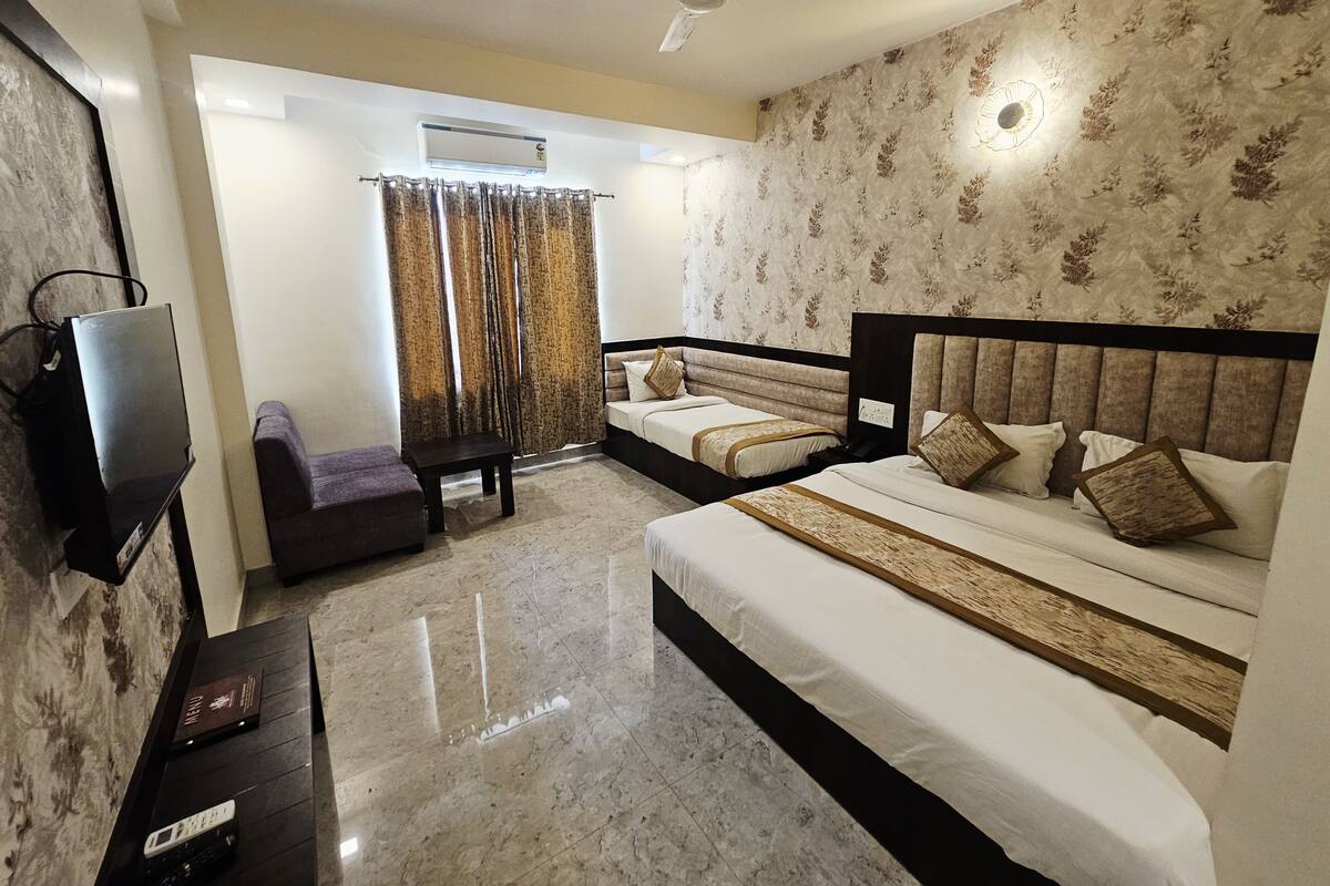 A hotel room with a bed, a sofa, a TV, a ceiling fan, and an air conditioning unit.