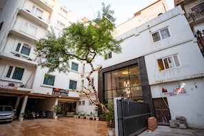 A hotel with a tiled courtyard, a tree, and a gated entrance. - Hotel KashiDham (Varanasi)