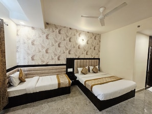 A bedroom with two beds, a ceiling fan, and patterned wallpaper. - Hotel KashiDham (Varanasi)