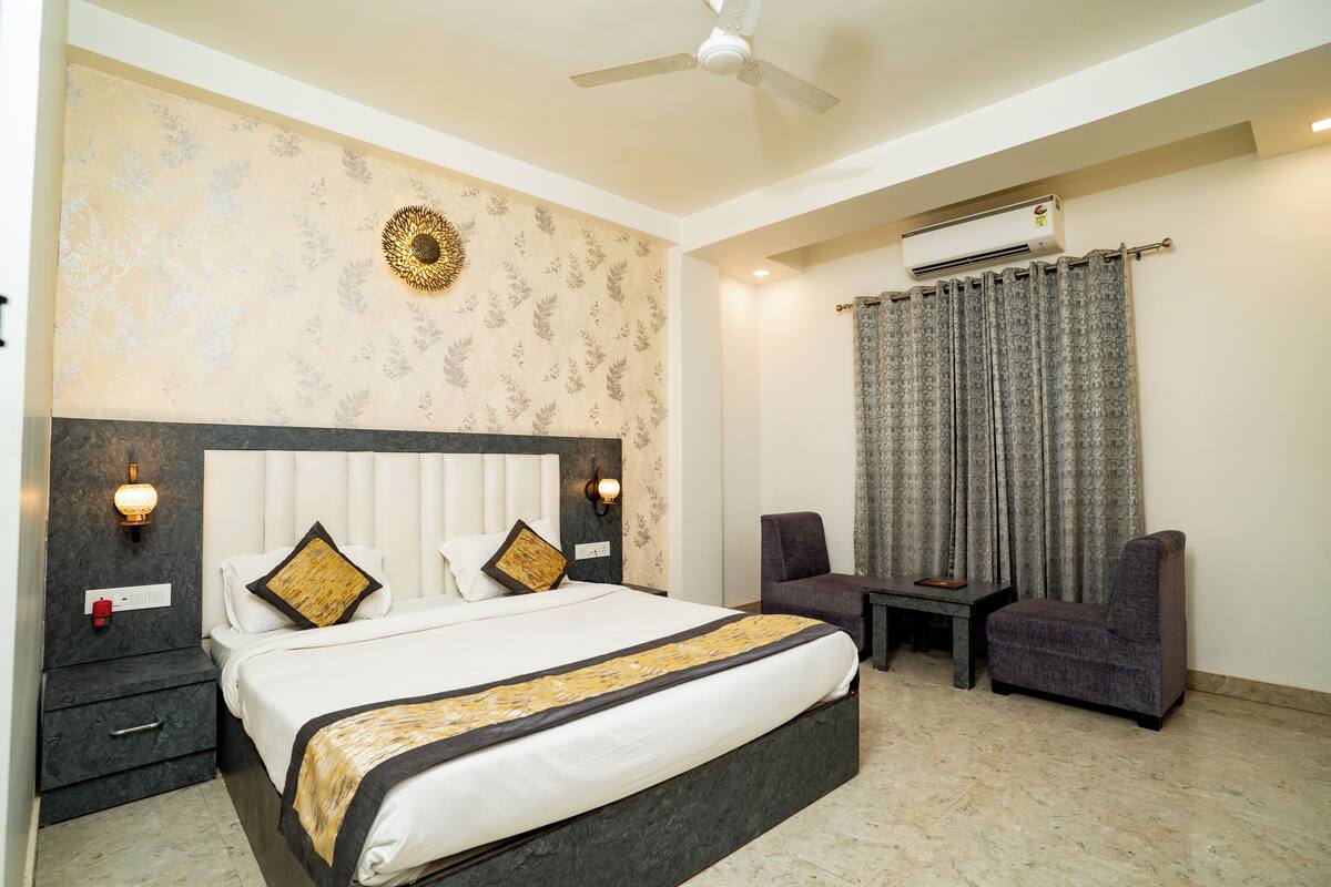 A hotel room with a bed, a chair, a table, a ceiling fan, and an air conditioning unit.
