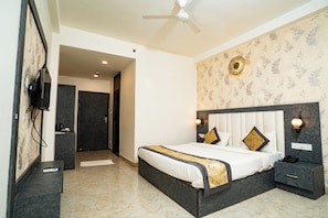 A bedroom with a bed, bedside table, nightstand, and a ceiling fan. - Hotel KashiDham (Varanasi)
