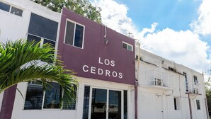 Un bâtiment portant une enseigne indiquant « Los Cedros », avec une façade blanche, de grandes fenêtres et une petite entrée dotée d’une porte en verre.