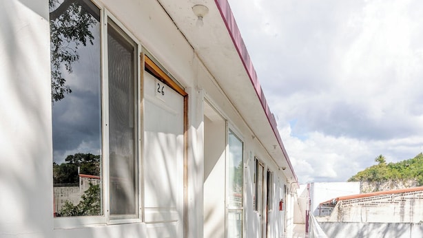 Un couloir aux murs blancs, avec un toit rouge et une fenêtre portant le numéro 26.