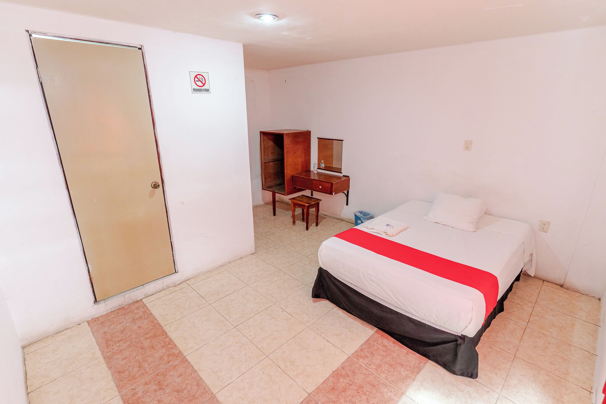 A hotel room with a bed, a desk, a chair, a wardrobe, and a no-smoking sign.