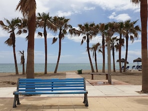 Ein Strand mit einer blauen Bank, Palmen und Strandstühlen.