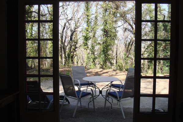 Blick durch ein Fenster auf einen Tisch und Stühle, umgeben von Bäumen.
