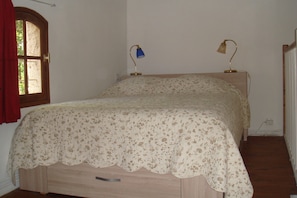 Ein Schlafzimmer mit einem Bett, zwei Nachttischlampen, einem Fenster mit Vorhängen und einer Heizung.