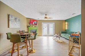 En stue med pejs, en grøn sofa, et spisebord med stole og en loftsvifte.
