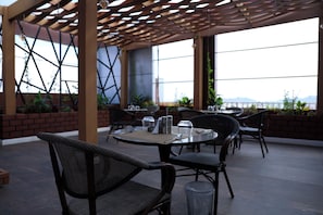 An outdoor seating area with tables and chairs, a pergola, and a view of the cityscape.