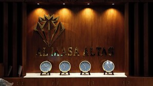 A reception desk with a wooden backdrop, a logo, and four clocks. - Al Masa Al Taj Hotel Apartments (Ha'il)
