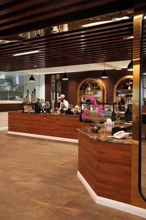 A hotel reception area with a wooden reception desk, a bar, and a counter with a phone and a vase of flowers. - Al Masa Al Taj Hotel Apartments (Ha'il)