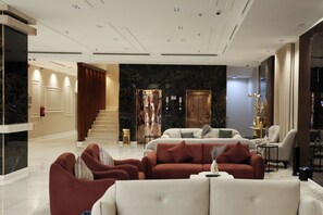 A spacious lobby with a marble reception desk, a staircase, and a seating area with sofas and armchairs.