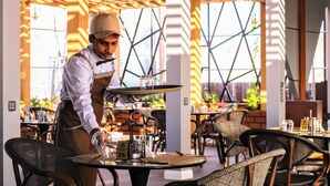 A waiter serving a table in a restaurant with a modern geometric ceiling and outdoor seating. - Al Masa Al Taj Hotel Apartments (Ha'il)