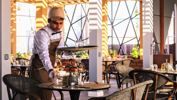 A waiter serving a table in a restaurant with a modern geometric ceiling and outdoor seating. - Al Masa Al Taj Hotel Apartments (Ha'il)