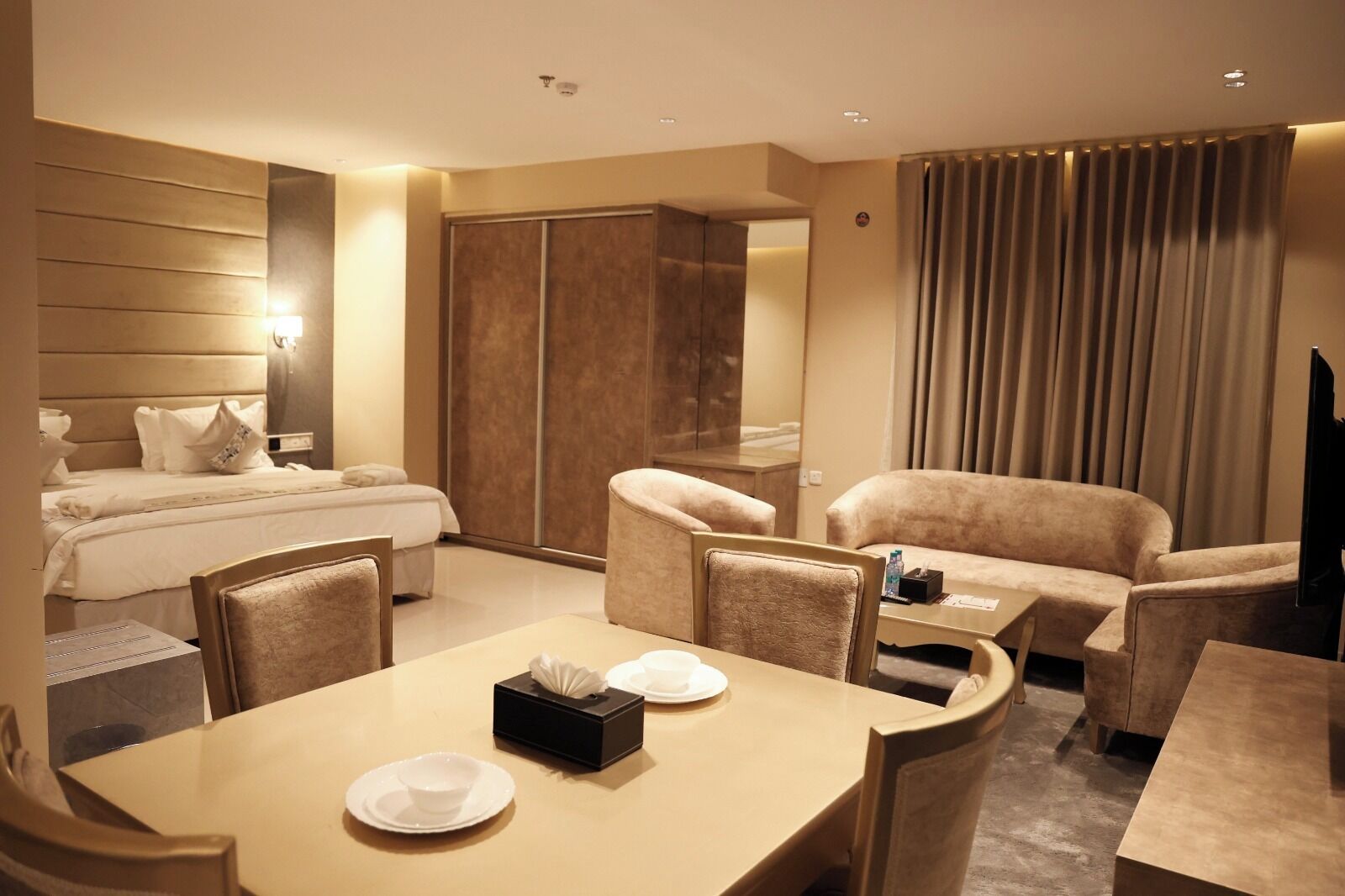 Een hotelkamer met een bed, een eettafel met stoelen, een bank, een televisie en een kledingkast.