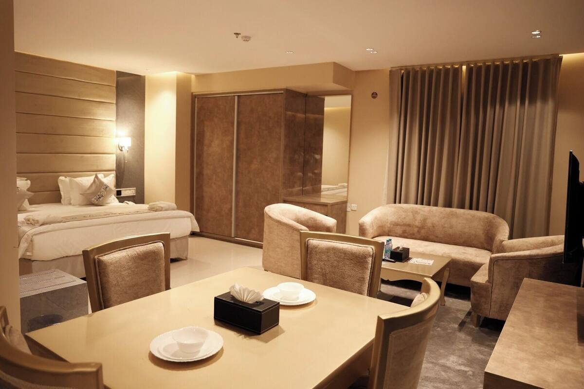 Quarto de hotel com cama, mesa de jantar com cadeiras, sofá, televisão e guarda-roupa.