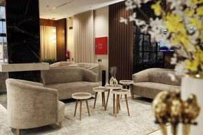 A modern lobby with sofas, round tables, and a marble column.