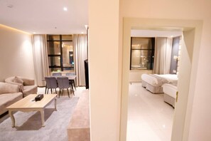 Een hotelkamer met een bank, een eettafel met stoelen, een kleine keukenhoek en een afzonderlijke slaapkamer met een bed.