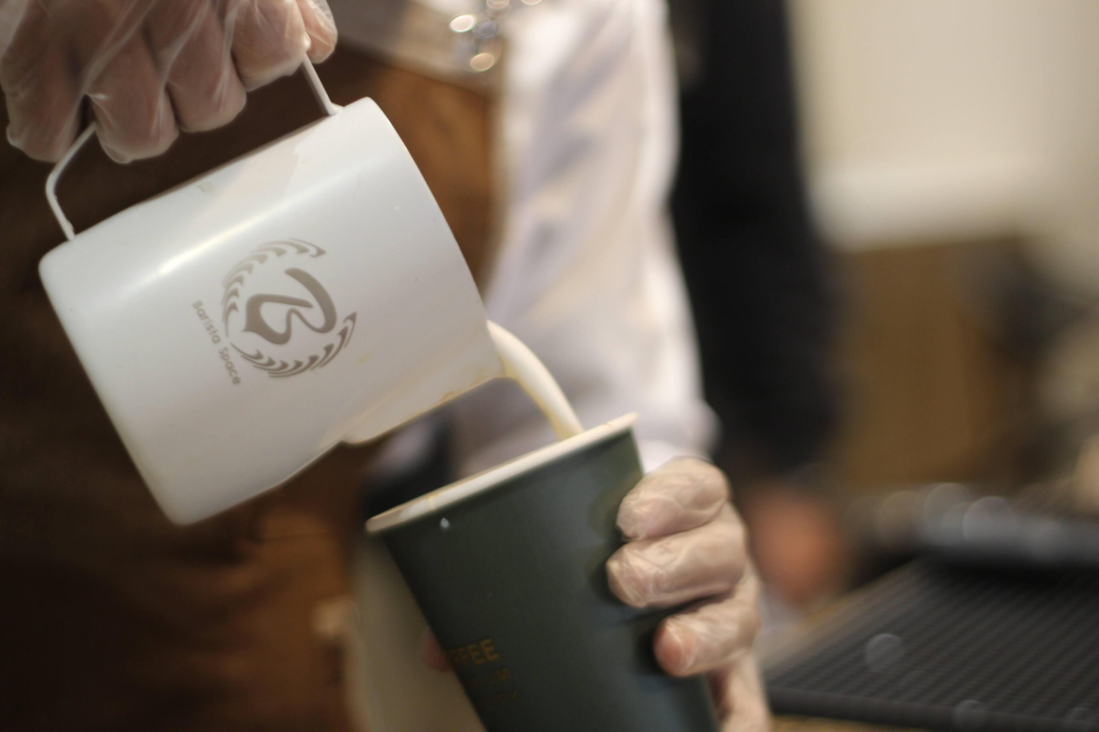 A person holding a white mug with a logo, pouring liquid into a green cup.