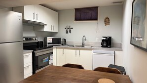 A compact kitchen with a refrigerator, microwave, stove, oven, sink, and coffee maker. There is a wooden dining table with chairs. - Bright 2BR BSMT Suite NR UofC n Foothills Hospital (Calgary)