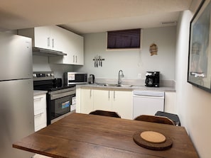 A compact kitchen with a refrigerator, microwave, stove, oven, sink, and coffee maker. There is a wooden dining table with chairs.
