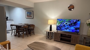 A living room with a TV, wooden furniture, a dining area, and a kitchen in the background. - Bright 2BR BSMT Suite NR UofC n Foothills Hospital (Calgary)