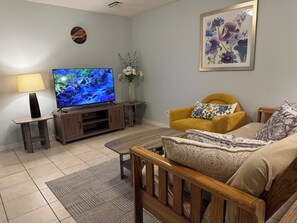 A living room with a TV, wooden furniture, a yellow armchair, and a floral painting.
