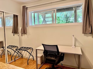 Una habitación con un escritorio blanco, una silla de oficina negra, un espejo grande y una ventana con cortinas.