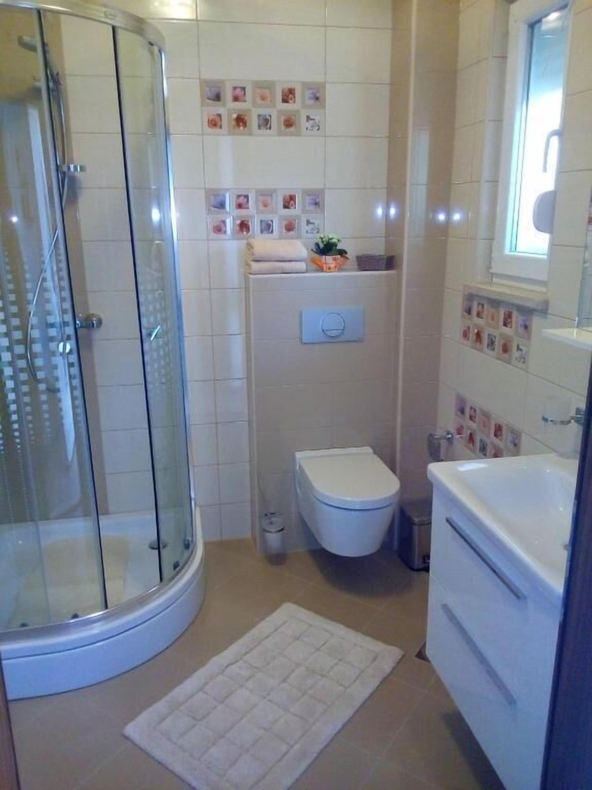 A bathroom with a glass shower enclosure, a toilet, a sink, and a mirror.