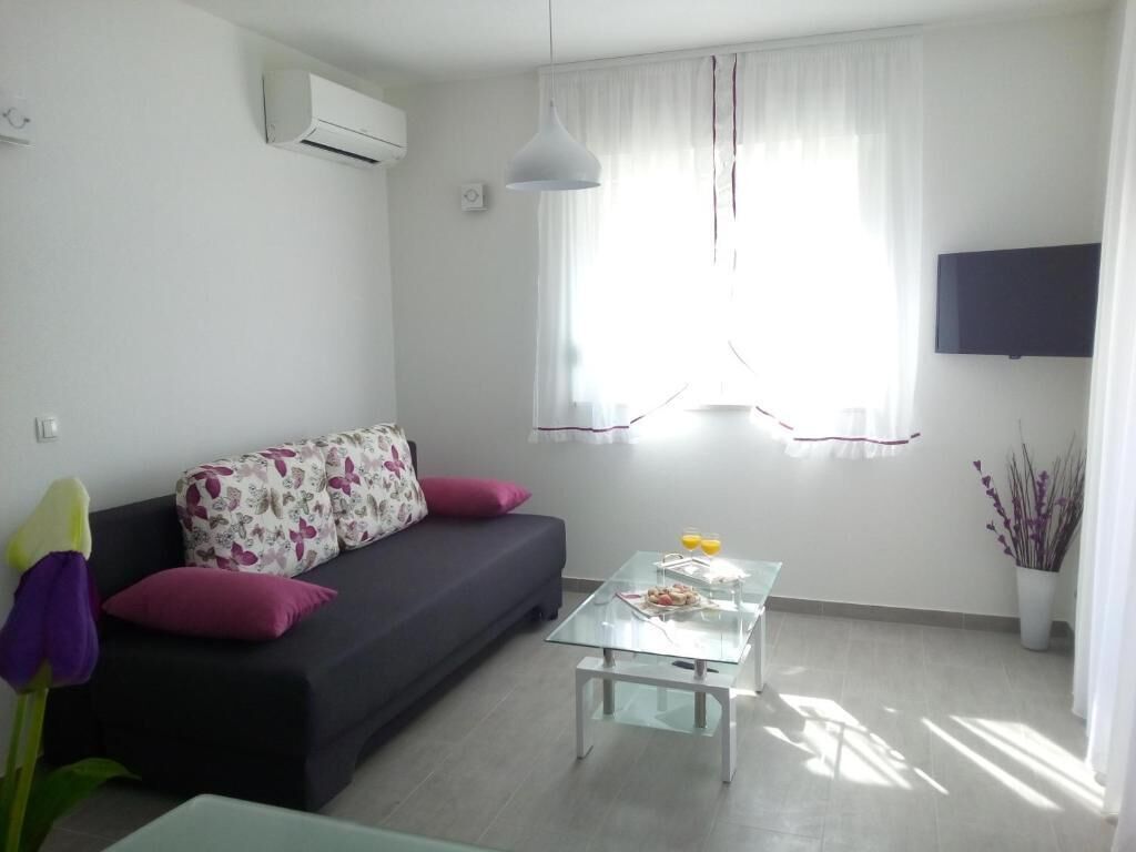 A living room with a sofa, a glass coffee table, a flat-screen TV, and a window with curtains.