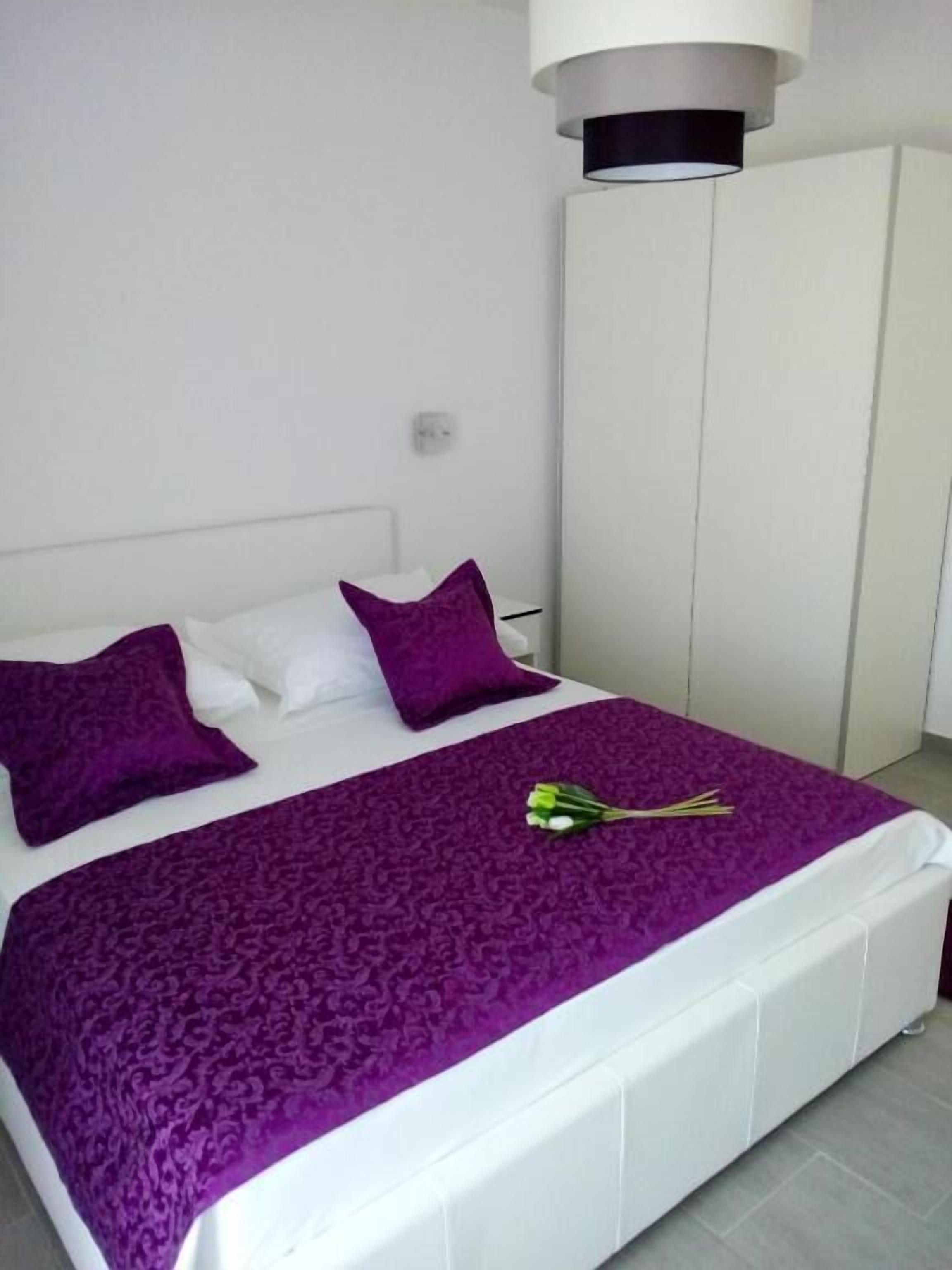 A bed with a white headboard, a purple bedspread, and two purple pillows.