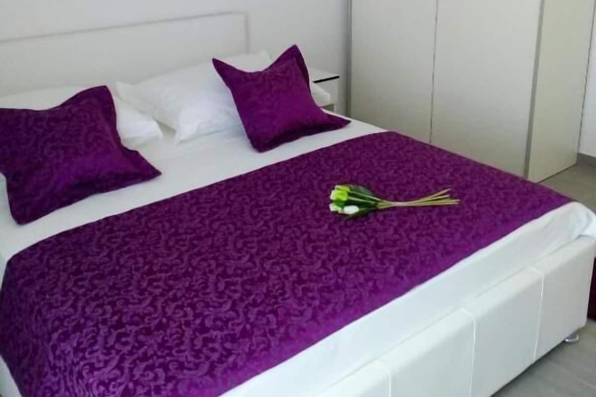 Una cama con cabecera blanca, colcha morada y dos almohadas moradas.