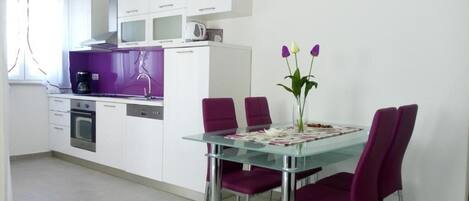Una cocina moderna con armarios blancos, una mesa de comedor de vidrio y sillas moradas.