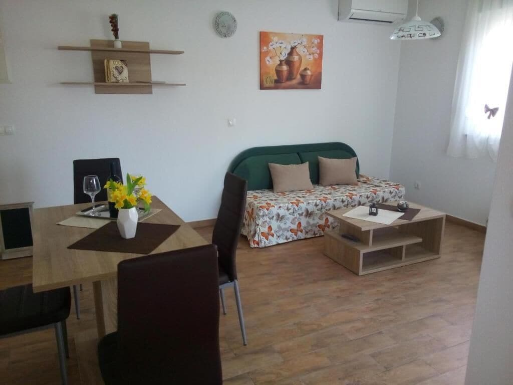 Una sala de estar con un sofá, una mesa de comedor con sillas, una mesa baja, una estantería y un cuadro en la pared.